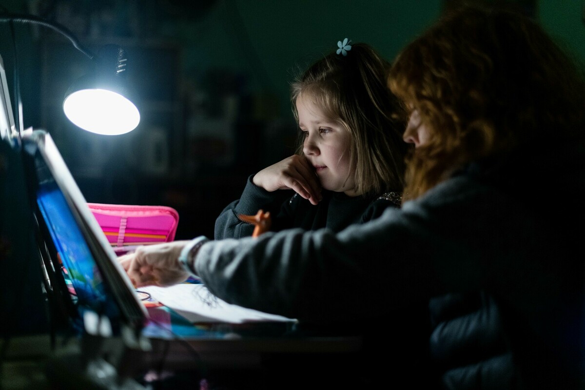 Mavka* helps Olesia* with her homework in their underground shelter in Kharkiv in November 2022. Image: Maciek Musialek/DEC.